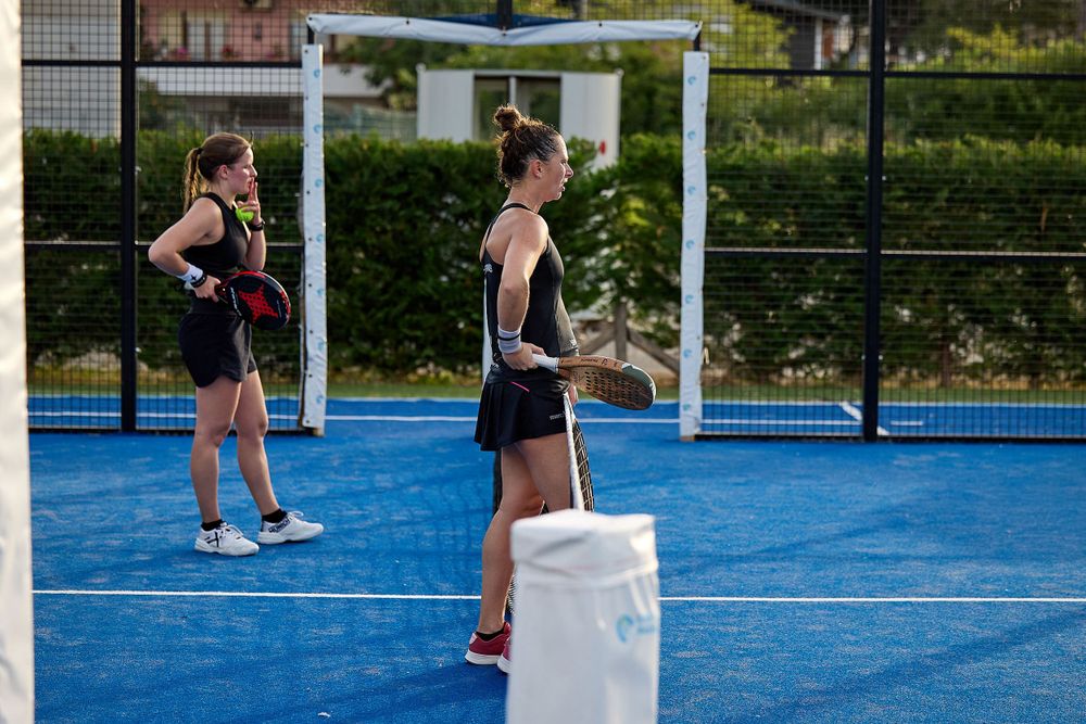 Two players stand on blue padel court during practice session.