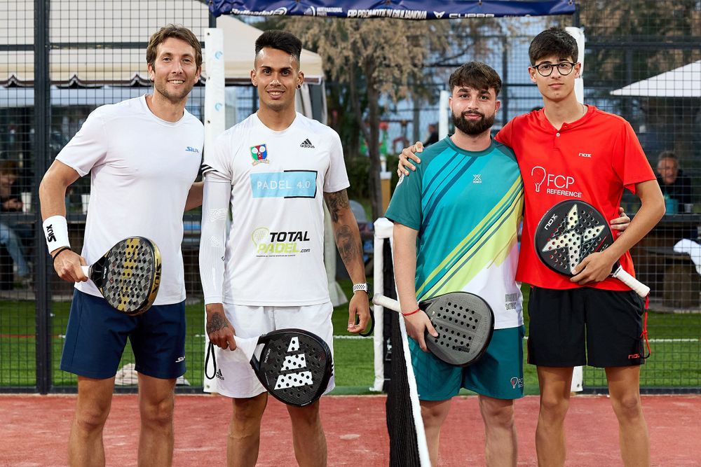 Four padel players posing with their rackets on court after match.