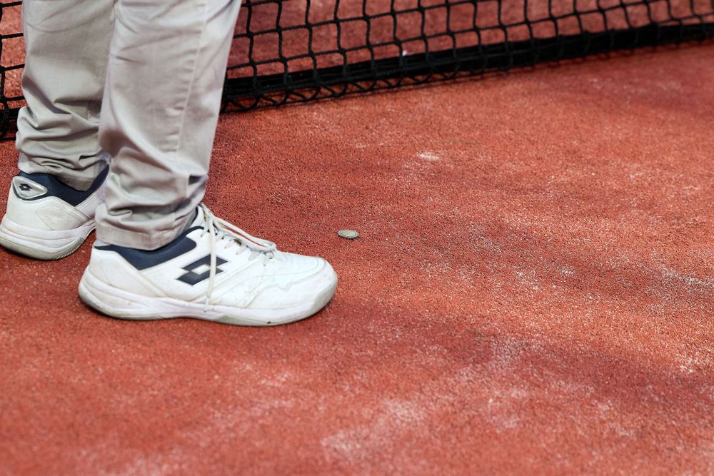 Close-up of white athletic shoes on red clay court surface.
