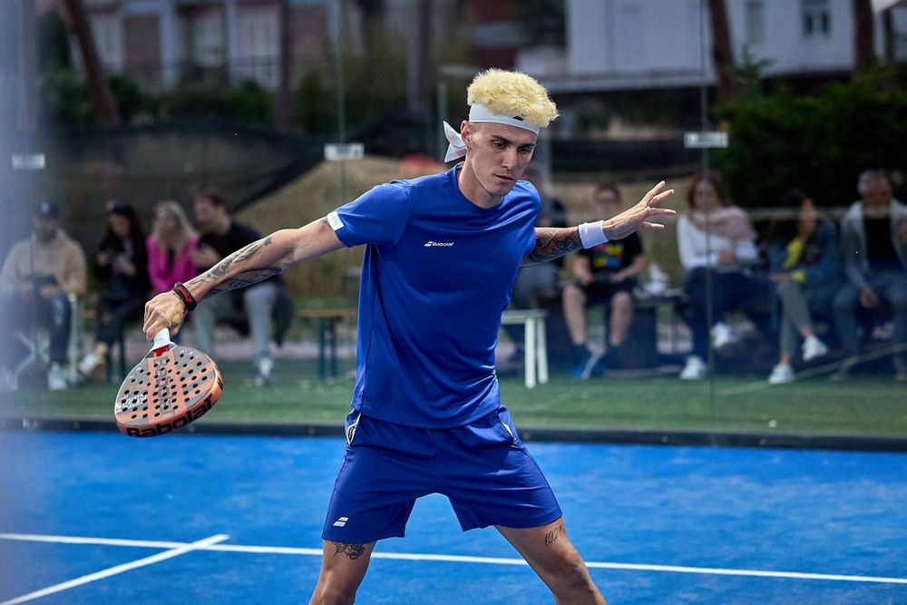 Player in blue uniform executing powerful forehand shot during padel match.