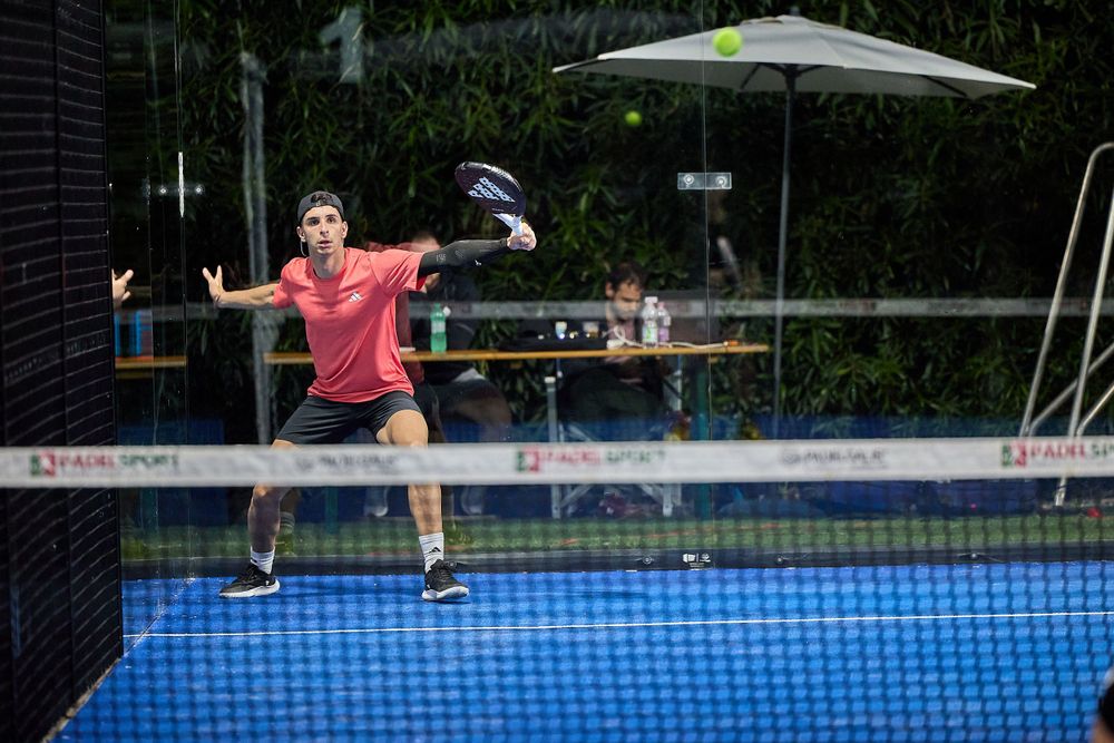 Player jumping to return shot on blue padel court during intense match.