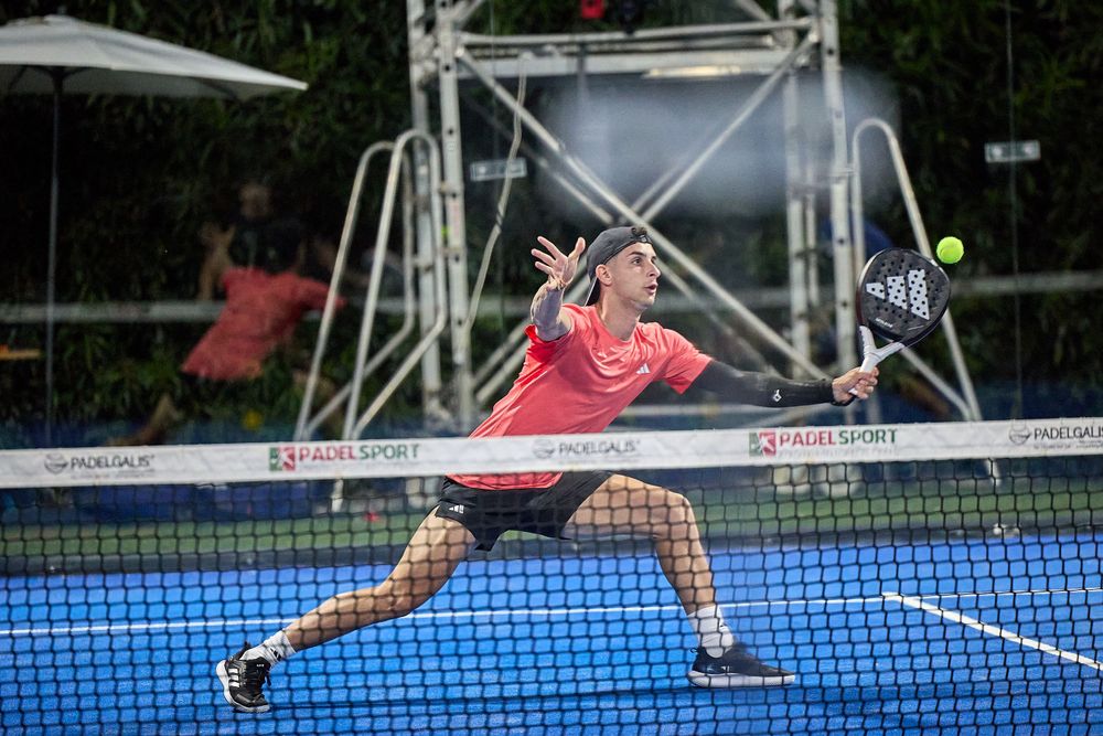Athletic player stretching wide to return shot on blue padel court.