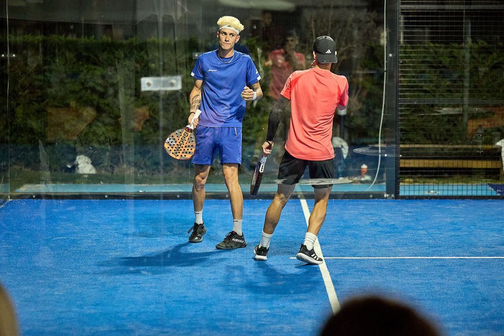 Two players compete in a padel match on a blue indoor court during gameplay.