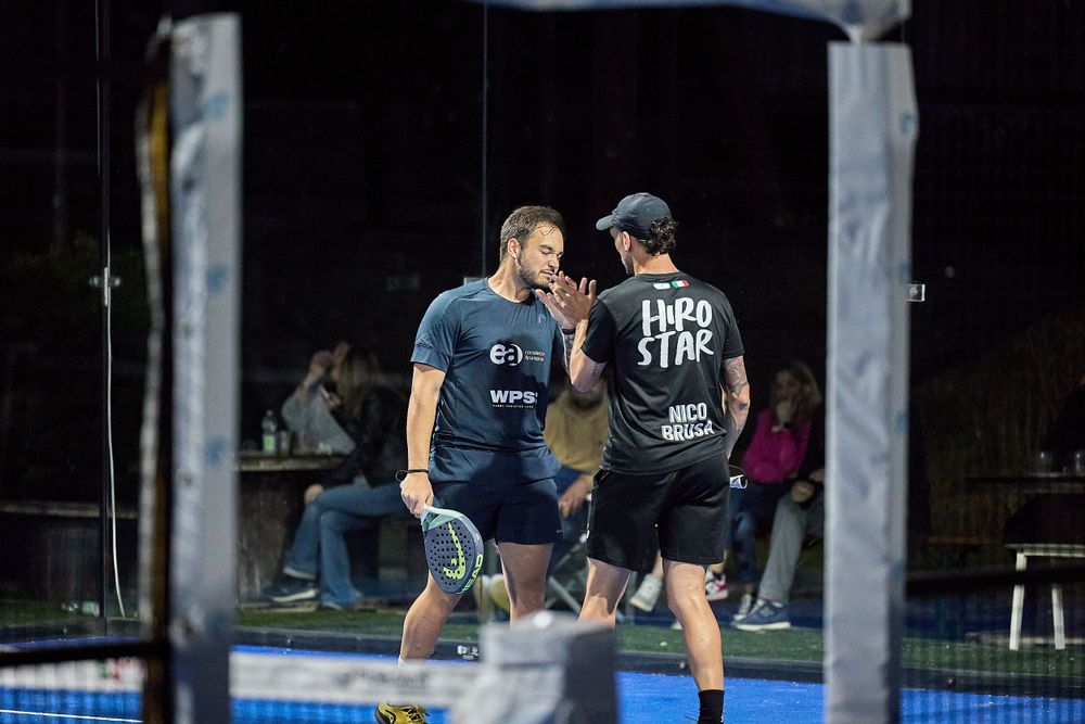 Two players celebrating point during nighttime padel match.