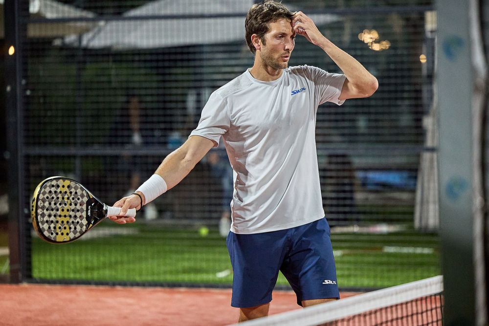 Player in white shirt practices forehand shot on outdoor tennis court during training session.