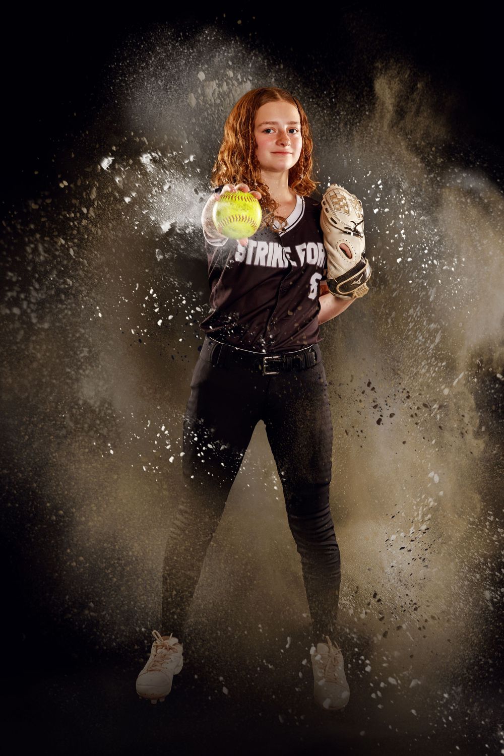 Dynamic sequence of softball pitcher in action against dramatic dark background with flying chalk dust effects.