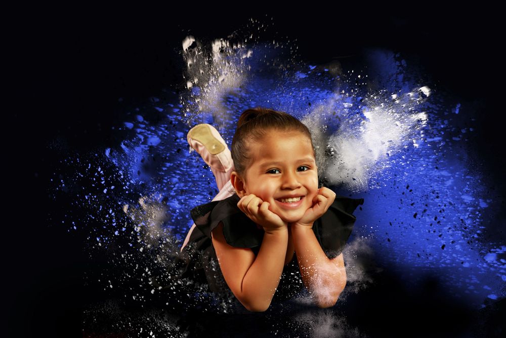Creative portrait against black background with vibrant blue powder explosion effect creating dramatic contrast.