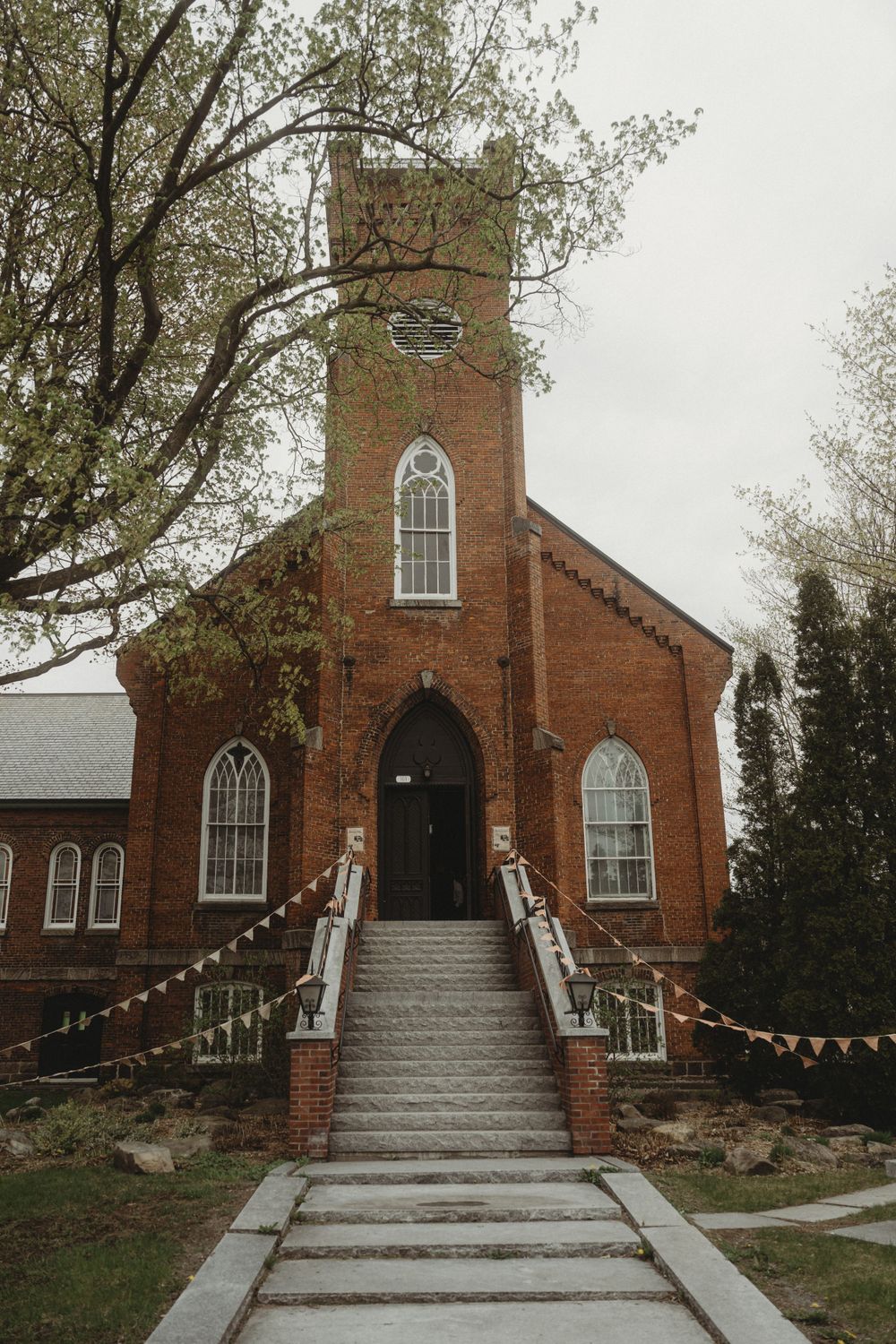 Historic red brick church with gothic windows decorated with string lights for wedding.