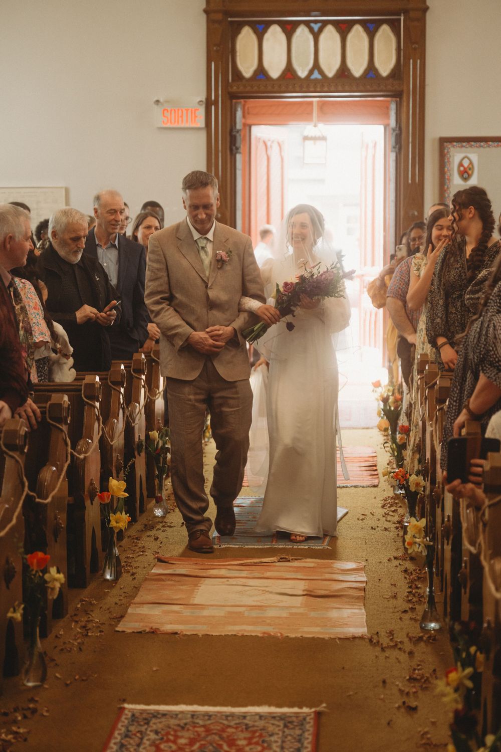 Traditional church wedding processional with flower-lined aisle and wooden pews.