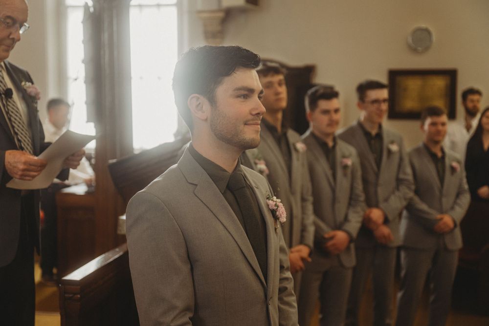 Groomsmen in grey suits stand in traditional church setting during ceremony.