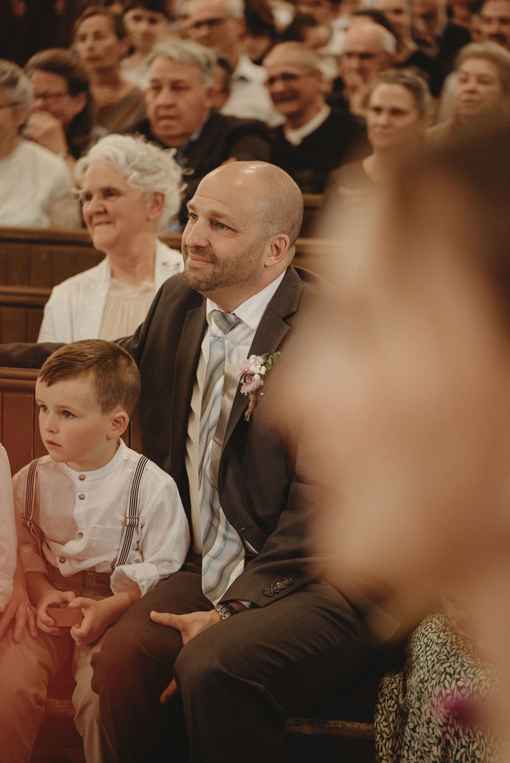 Wedding guests sit attentively in church pews during a ceremony.