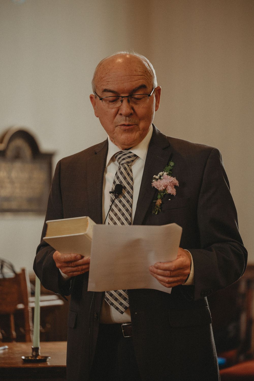 A person in a suit and tie reads from papers during what appears to be a formal ceremony.