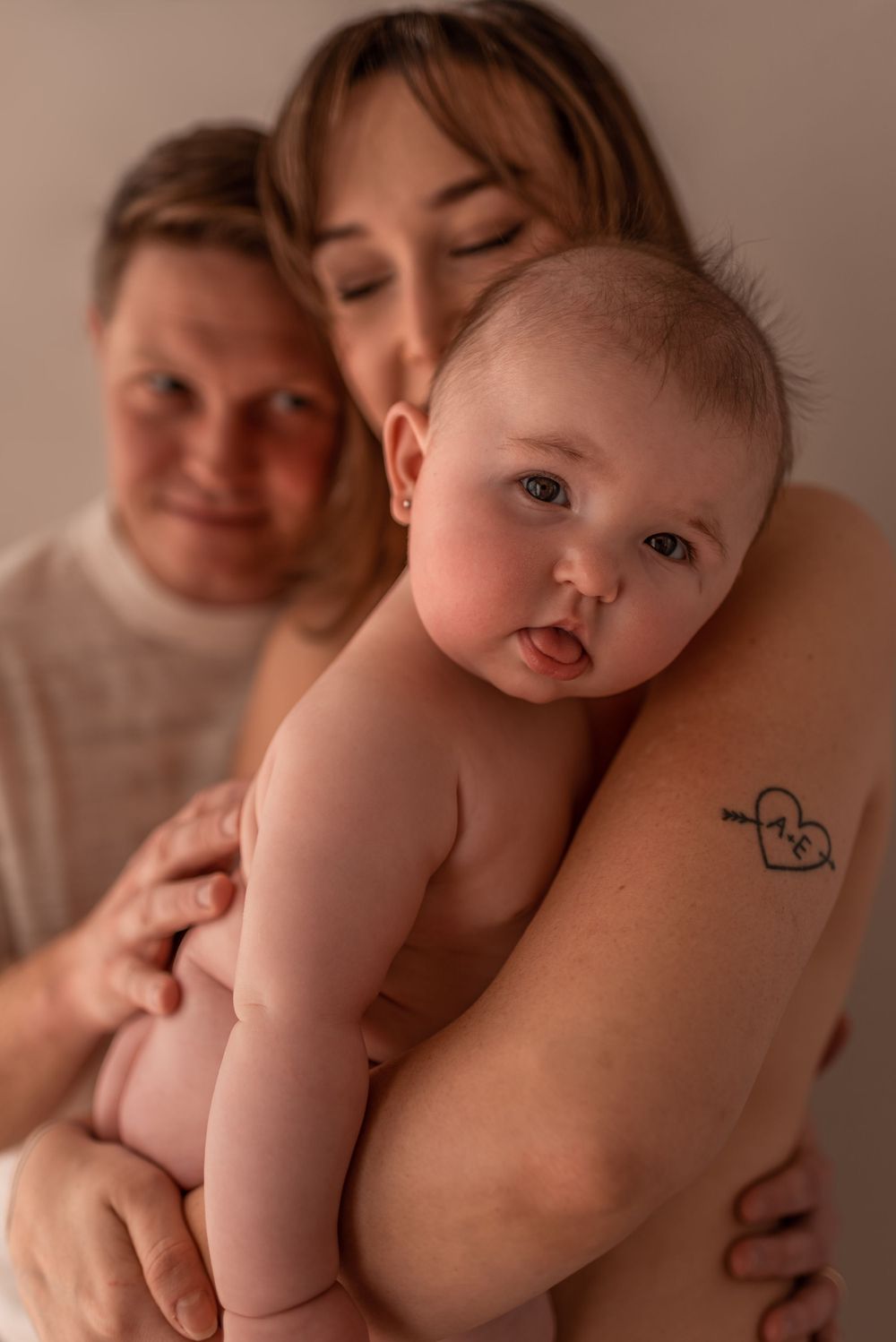 Family portrait showing loving embrace with baby in warm tones.