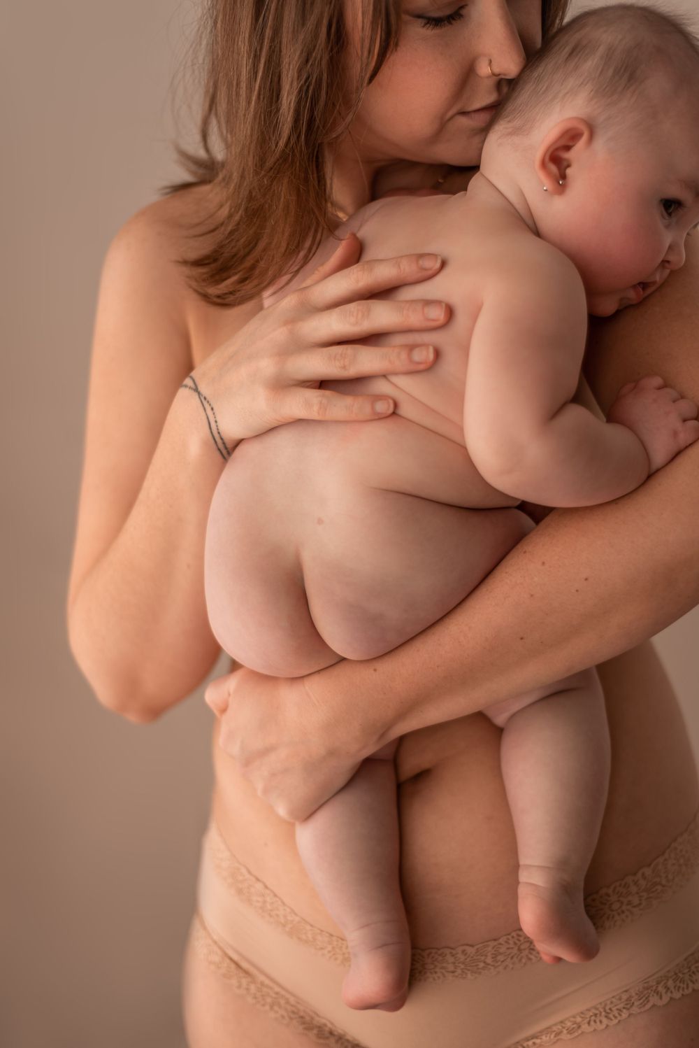 Intimate maternal photography showing gentle embrace with baby in neutral tones.