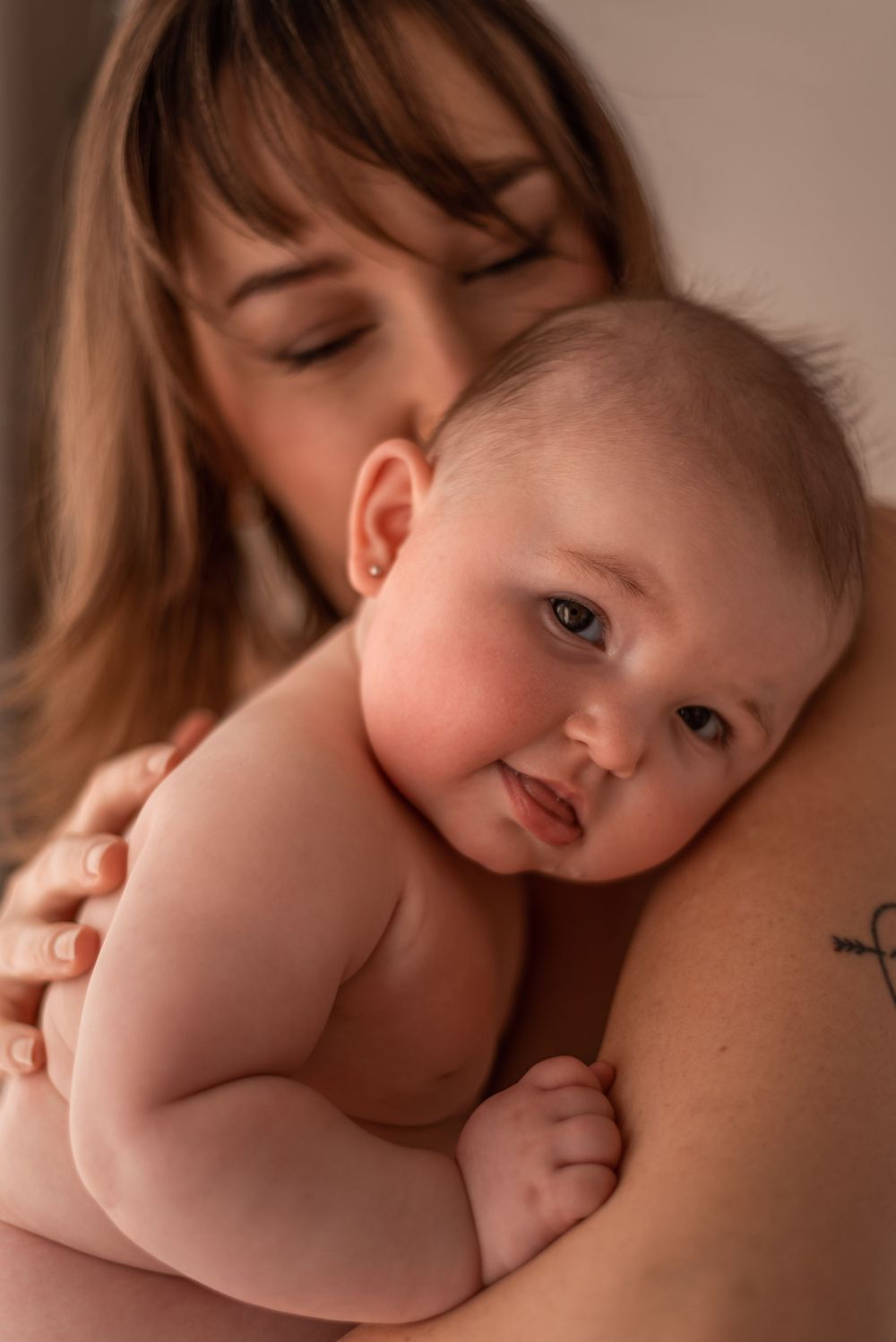 Intimate portrait showing tender moment between parent and baby in warm lighting.