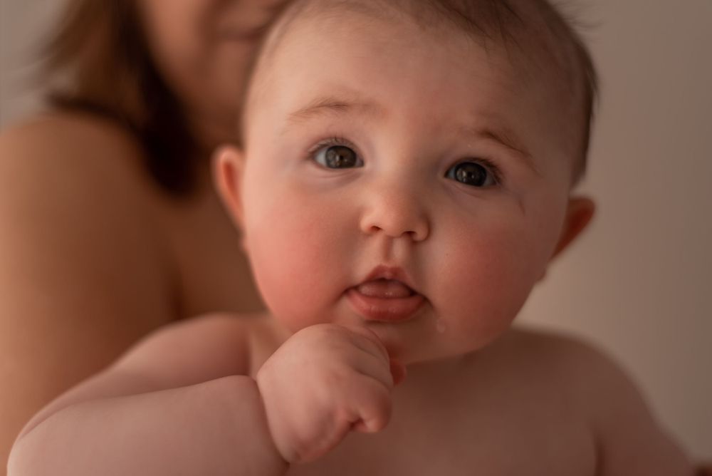 Close-up portrait of baby with rosy cheeks against warm background.