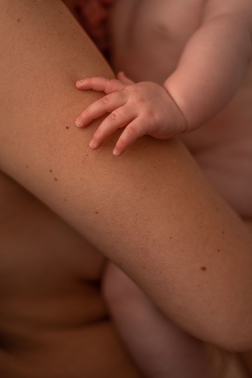 Close-up of tiny baby hand resting on skin in warm, intimate lighting.