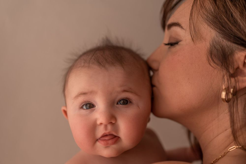 Tender close-up portrait of motherly love with gentle kiss on baby's cheek.