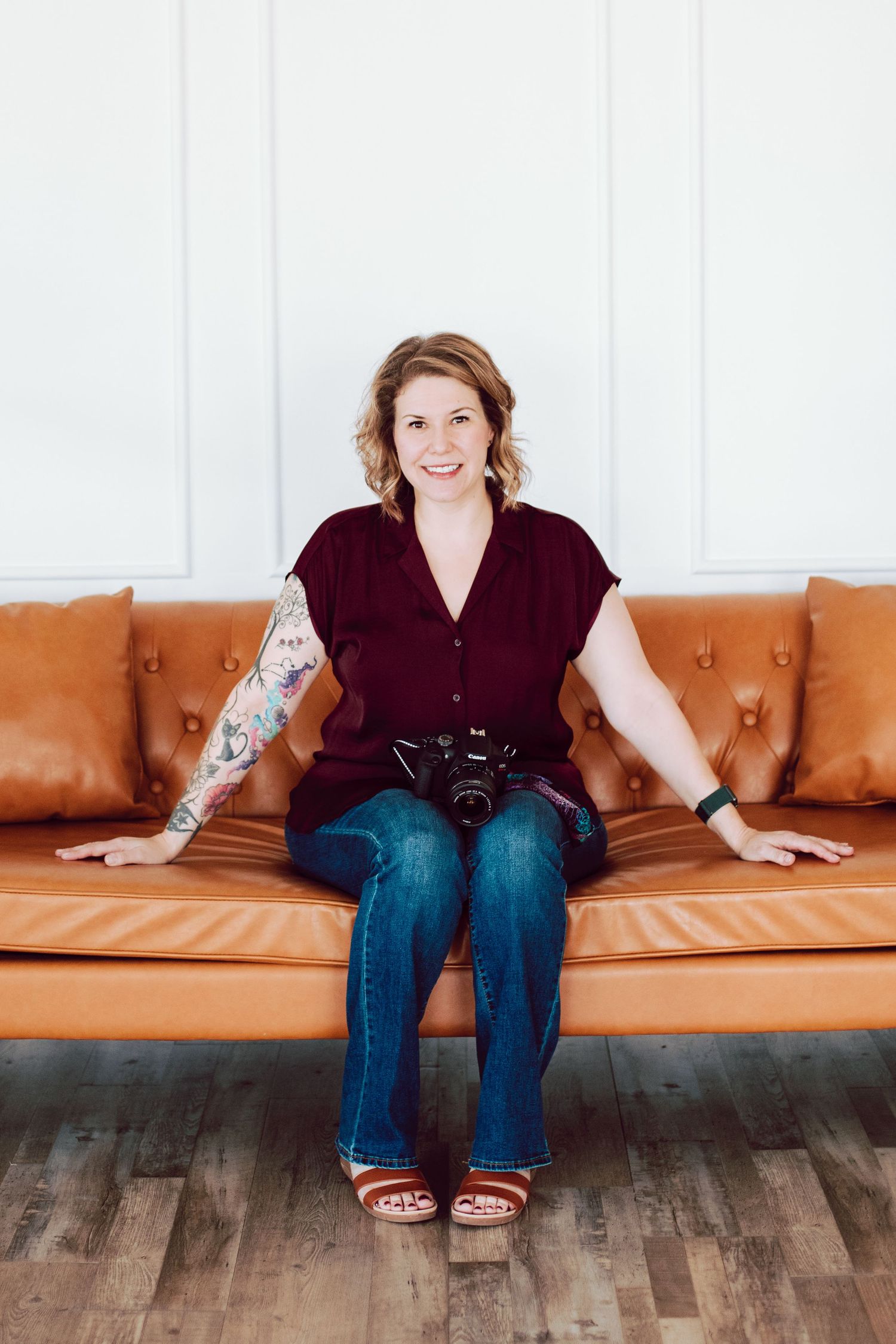 Person with camera sitting on tan leather couch against white wall.