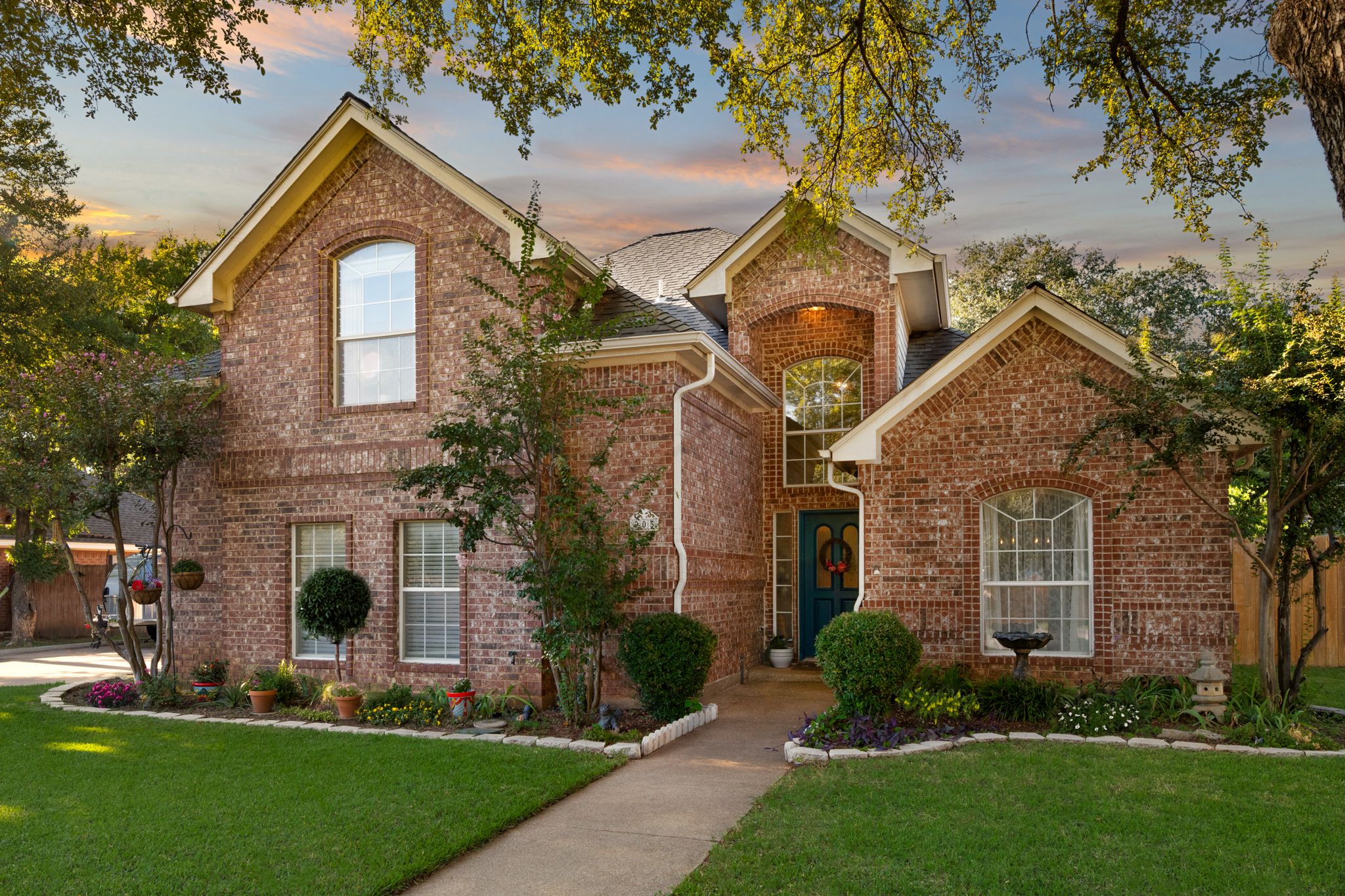 Two-story brick home with traditional architecture features manicured landscaping and a welcoming front entrance at sunset.