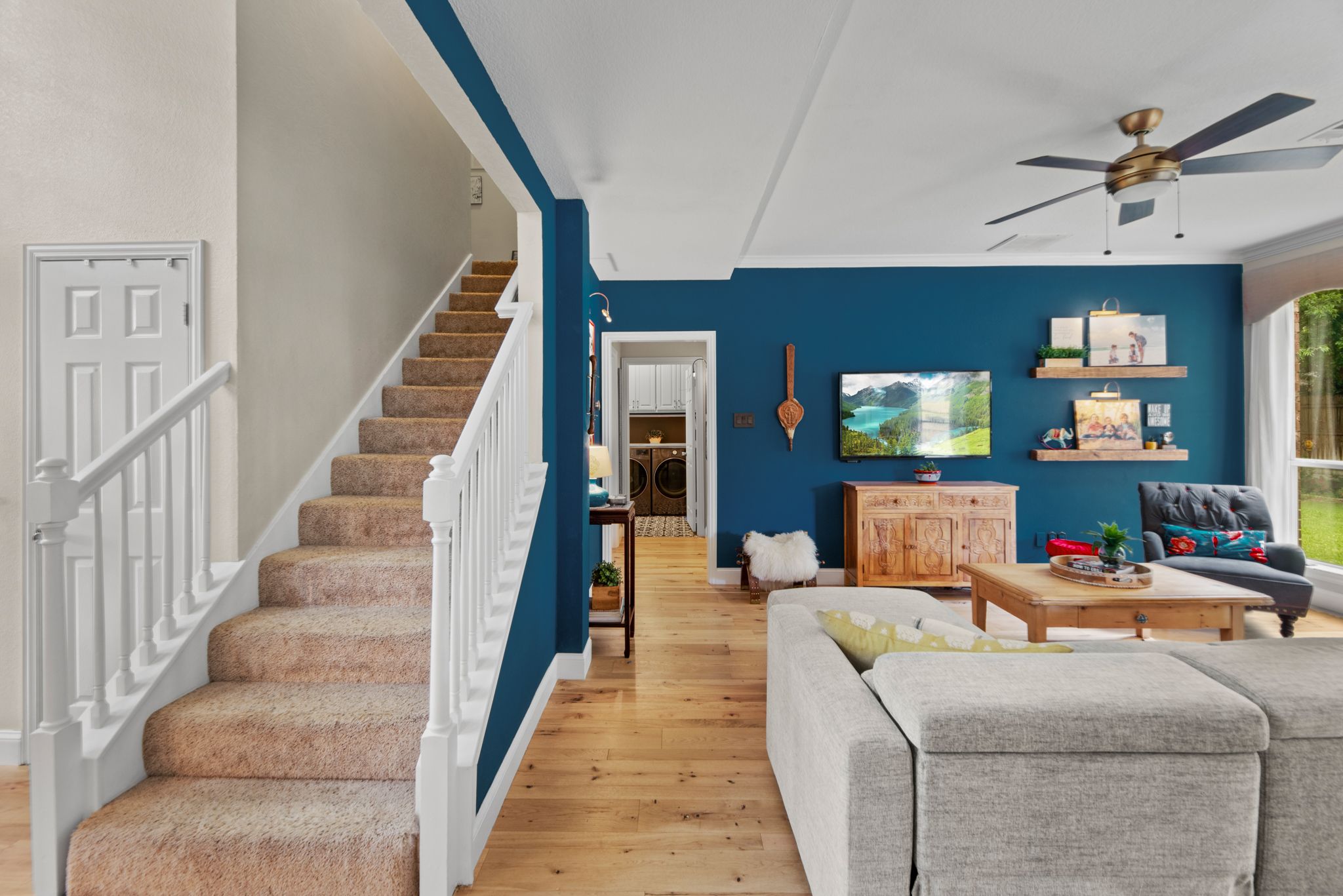 Modern living room with blue accent wall features carpeted stairs, hardwood floors and contemporary furnishings.