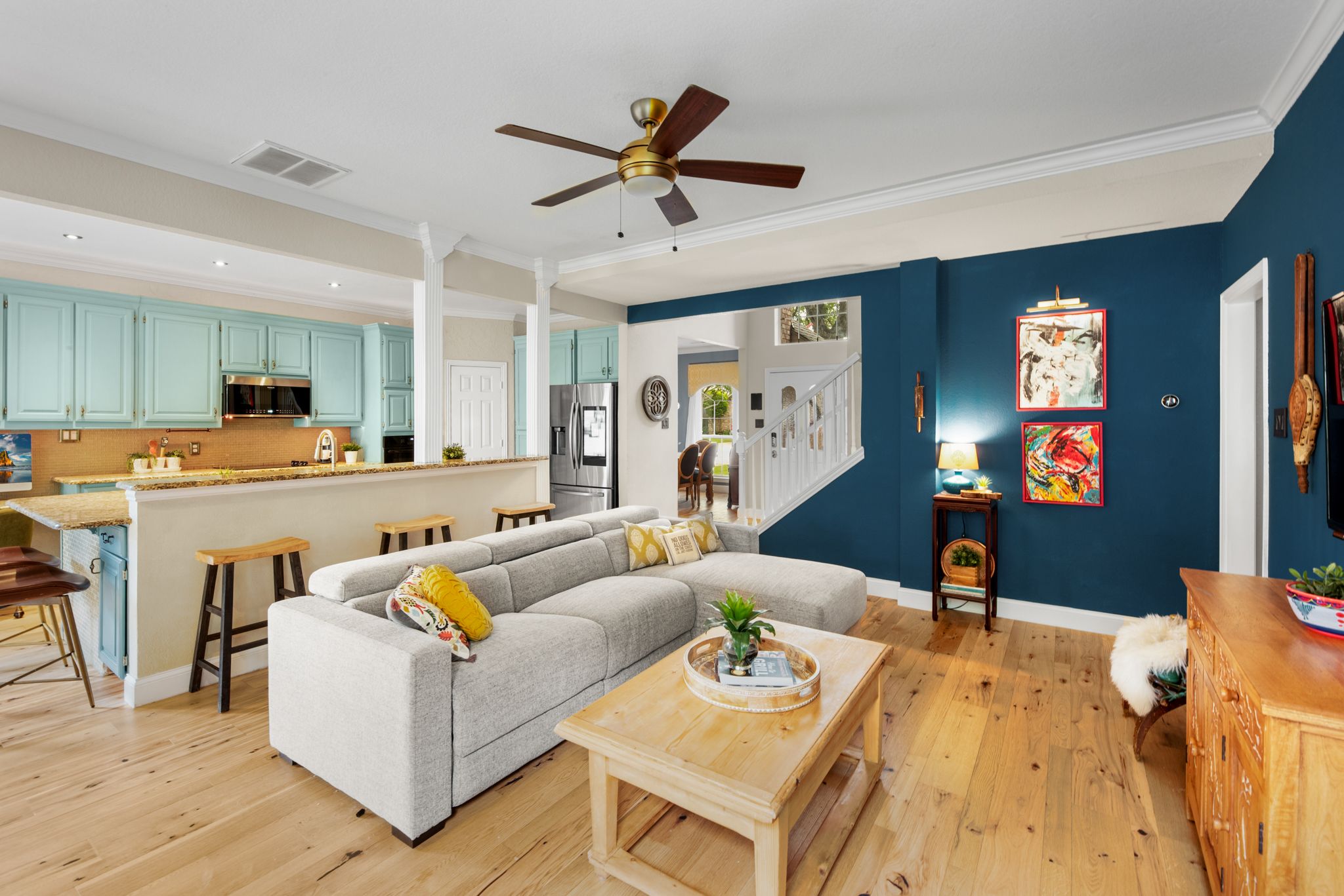 Modern living area with wood floors, ceiling fan, and teal kitchen cabinets visible in the background.