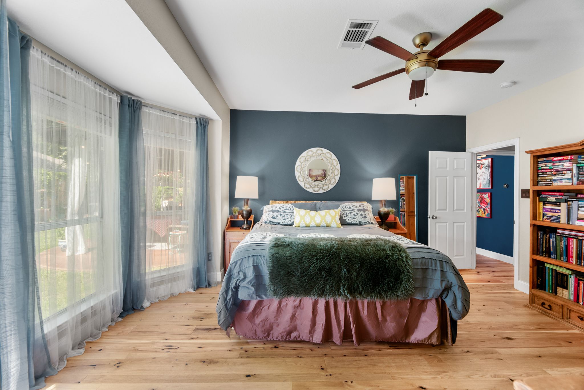 Spacious bedroom with navy blue accent wall, vaulted ceiling, and wooden floors features large windows with blue curtains.
