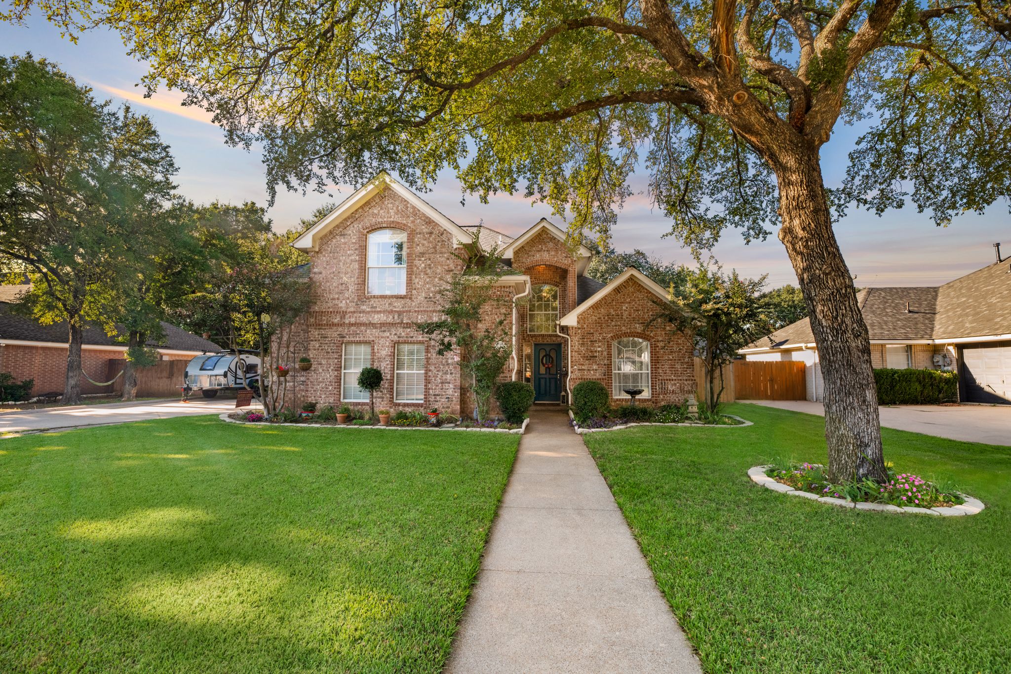 Elegant brick house with well-maintained lawn, mature trees, and concrete walkway leading to covered front entry.