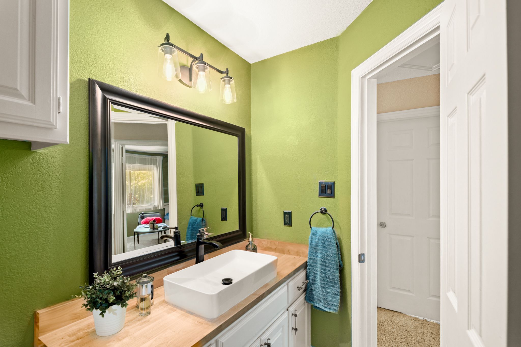 Modern bathroom with bright lime green walls, white cabinets, framed mirror, and a vessel sink on wood countertop.