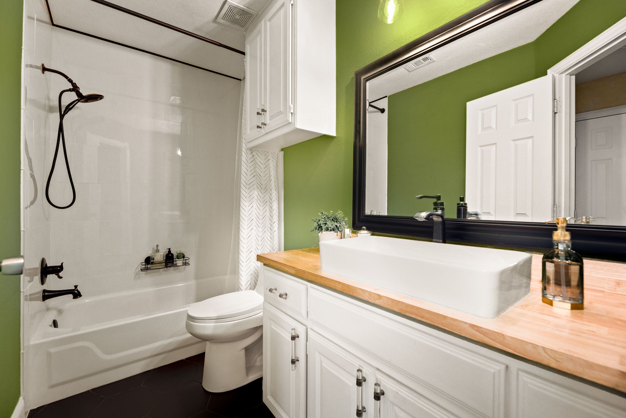 Modern bathroom with bright green walls, white cabinets, butcher block counter, dark granite sink and white shower tub combo.