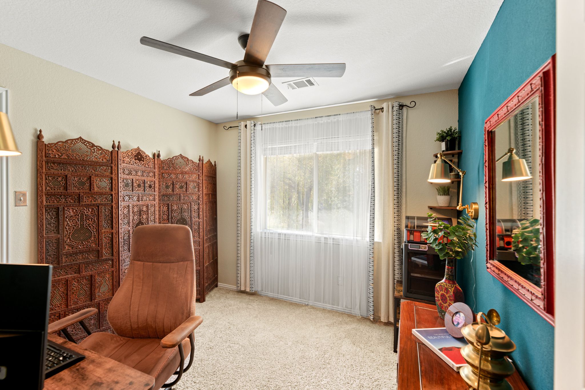 Bright room with brown folding screen, tan recliner chair, turquoise accent wall, ceiling fan and sheer curtains.