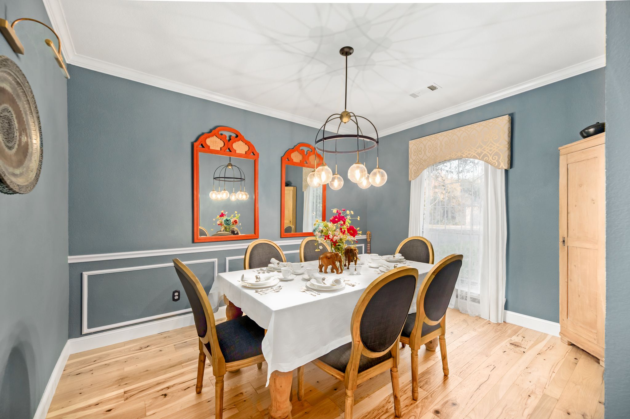 Modern dining room with blue-gray walls, wood floors, farmhouse table, and black upholstered chairs under pendant lighting.