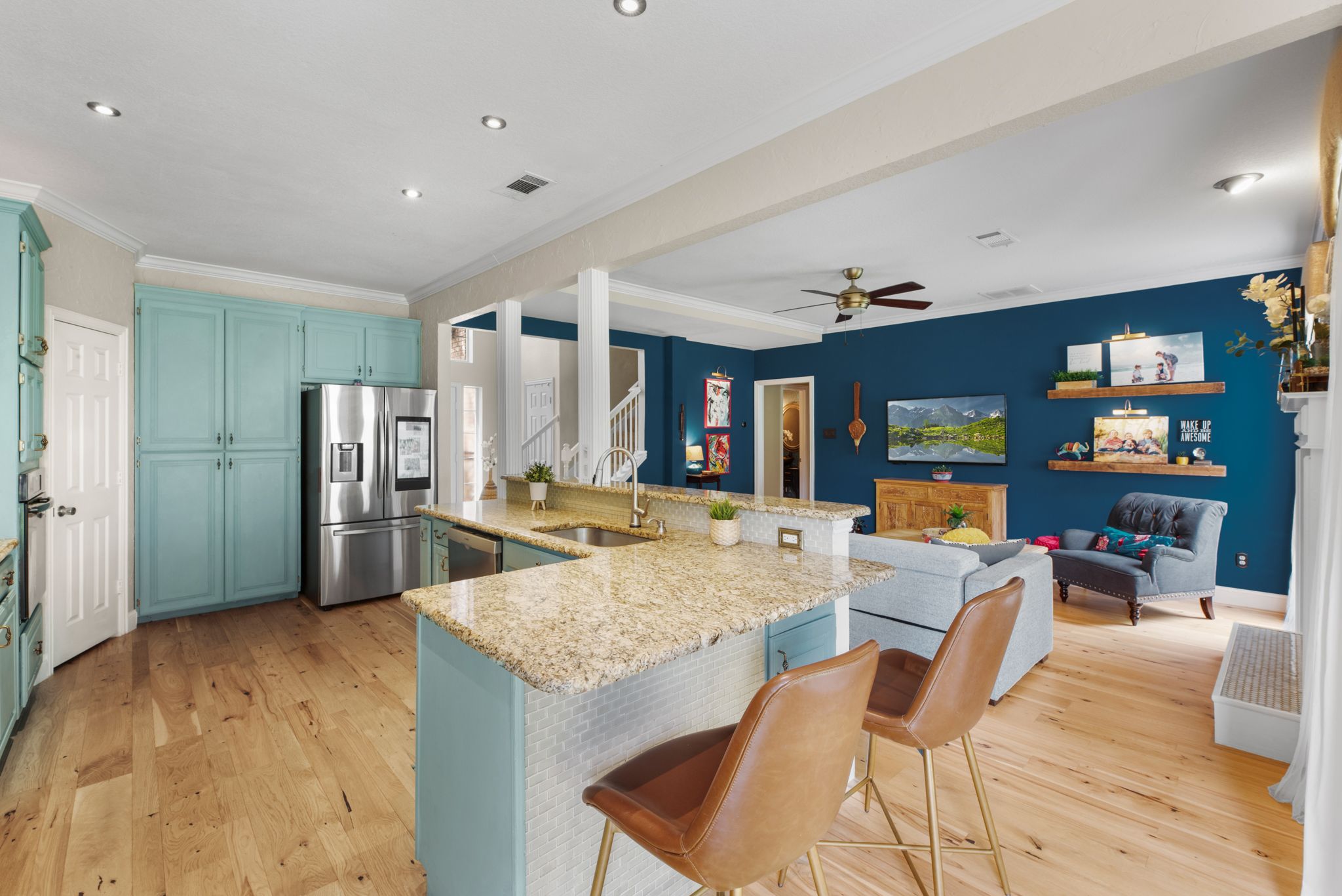 Open concept living space with hardwood floors, white walls, and teal accent walls featuring modern furnishings.