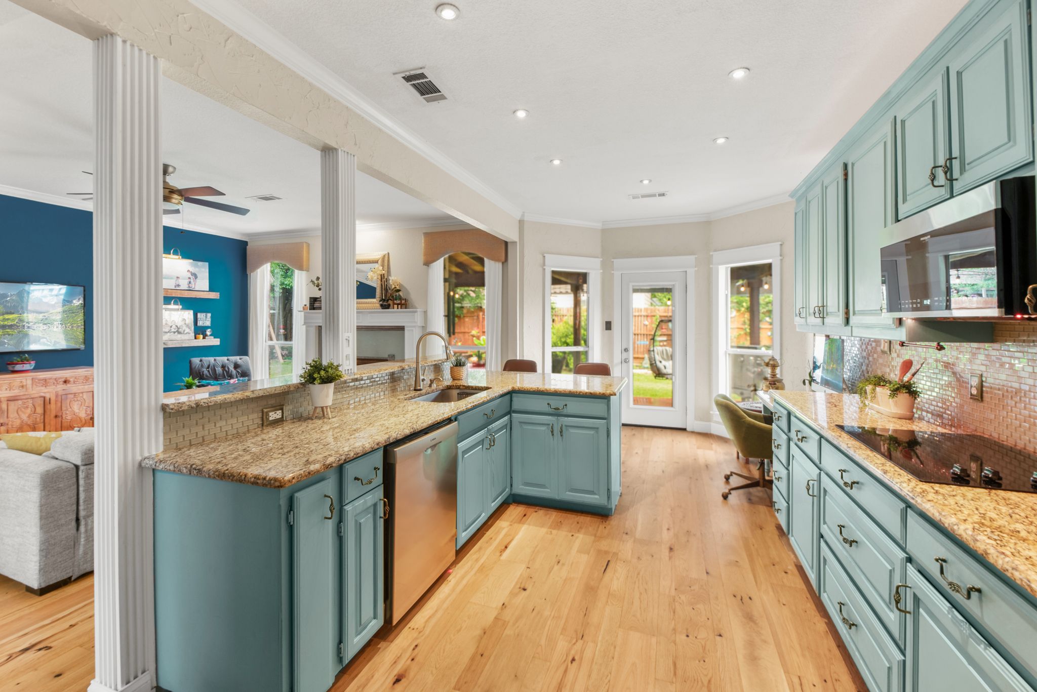 Modern kitchen featuring teal cabinets, granite countertops, hardwood floors and open-concept design with ample natural light.