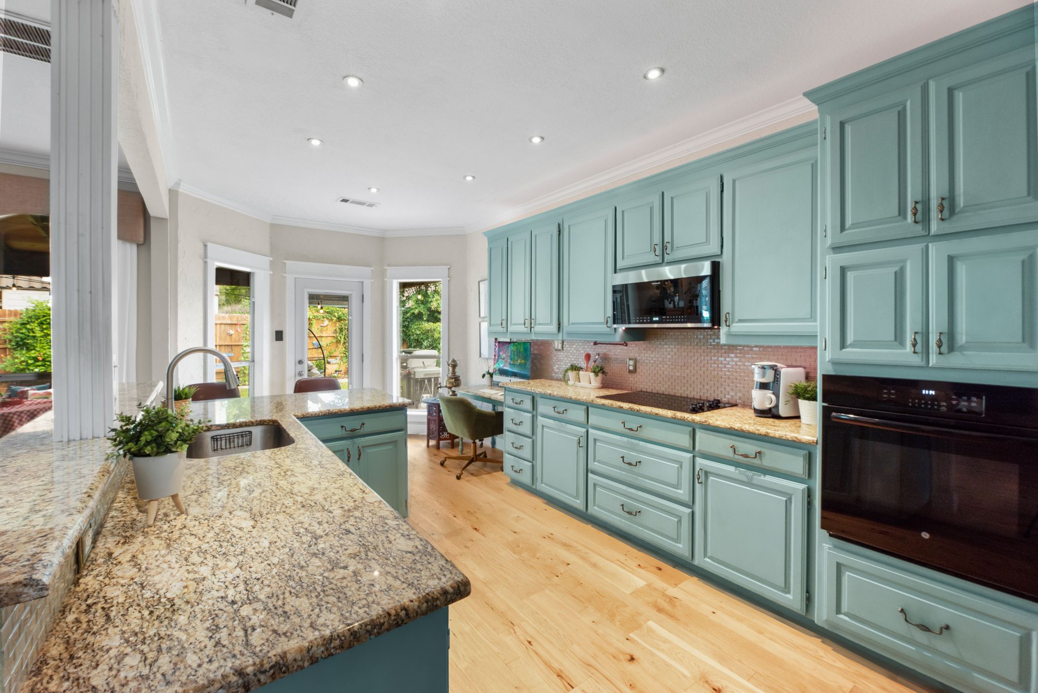 Modern kitchen with teal cabinets, granite countertops, hardwood floors and large windows offering natural light.