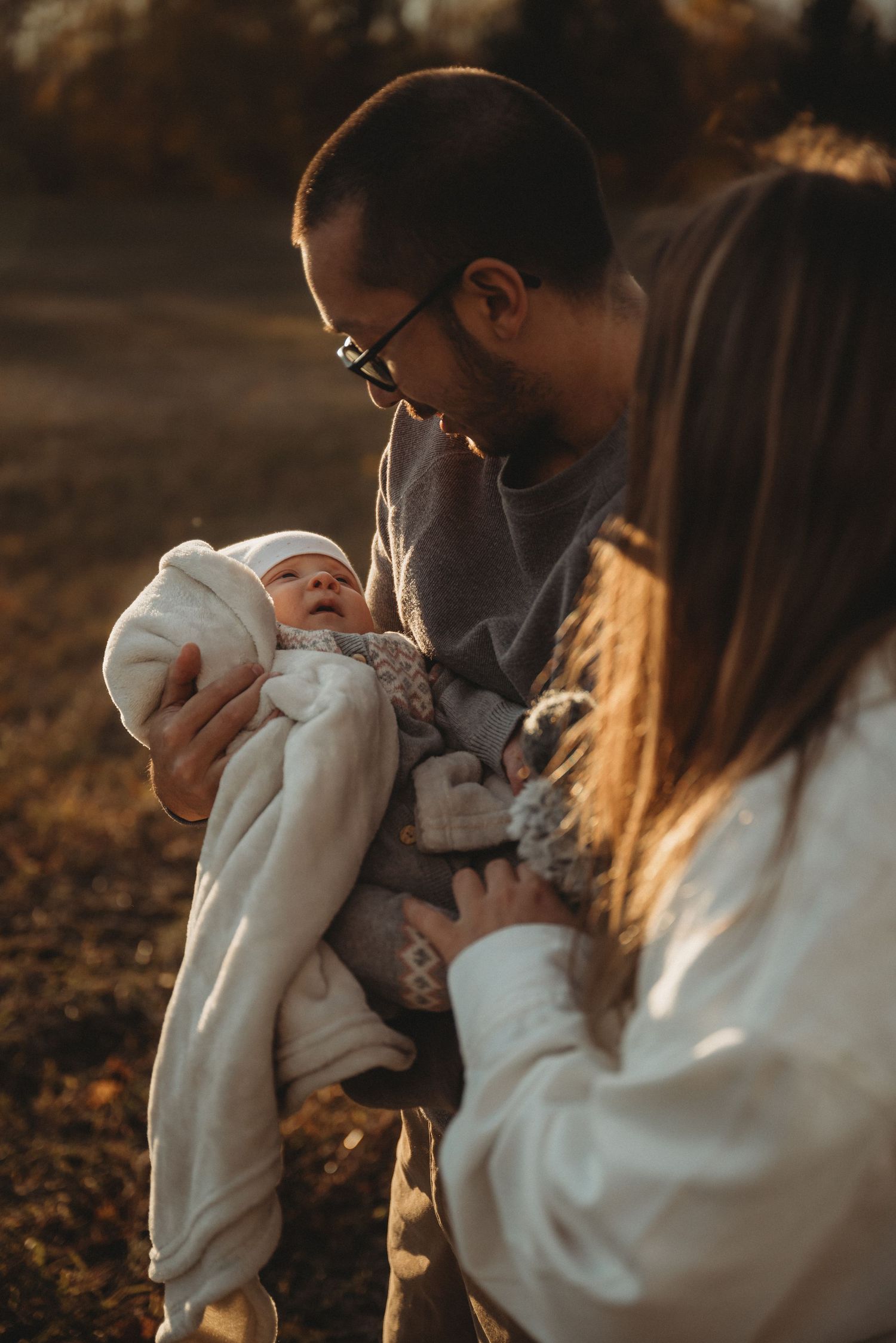 Parents admiring their swaddled newborn baby in golden sunset light.