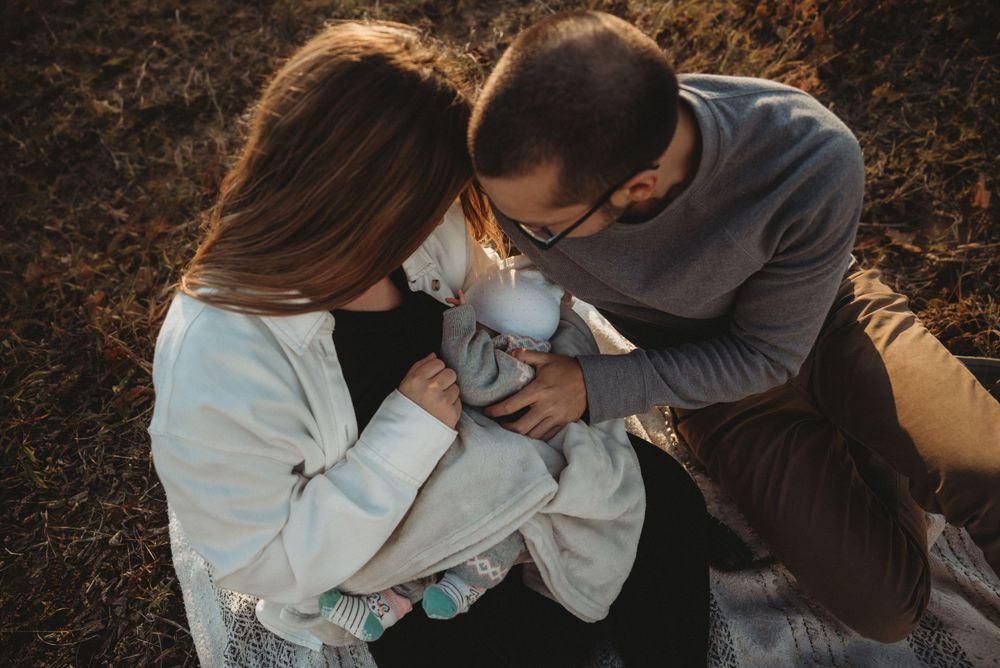 Parents lovingly gaze at their newborn baby wrapped in white blanket outdoors.
