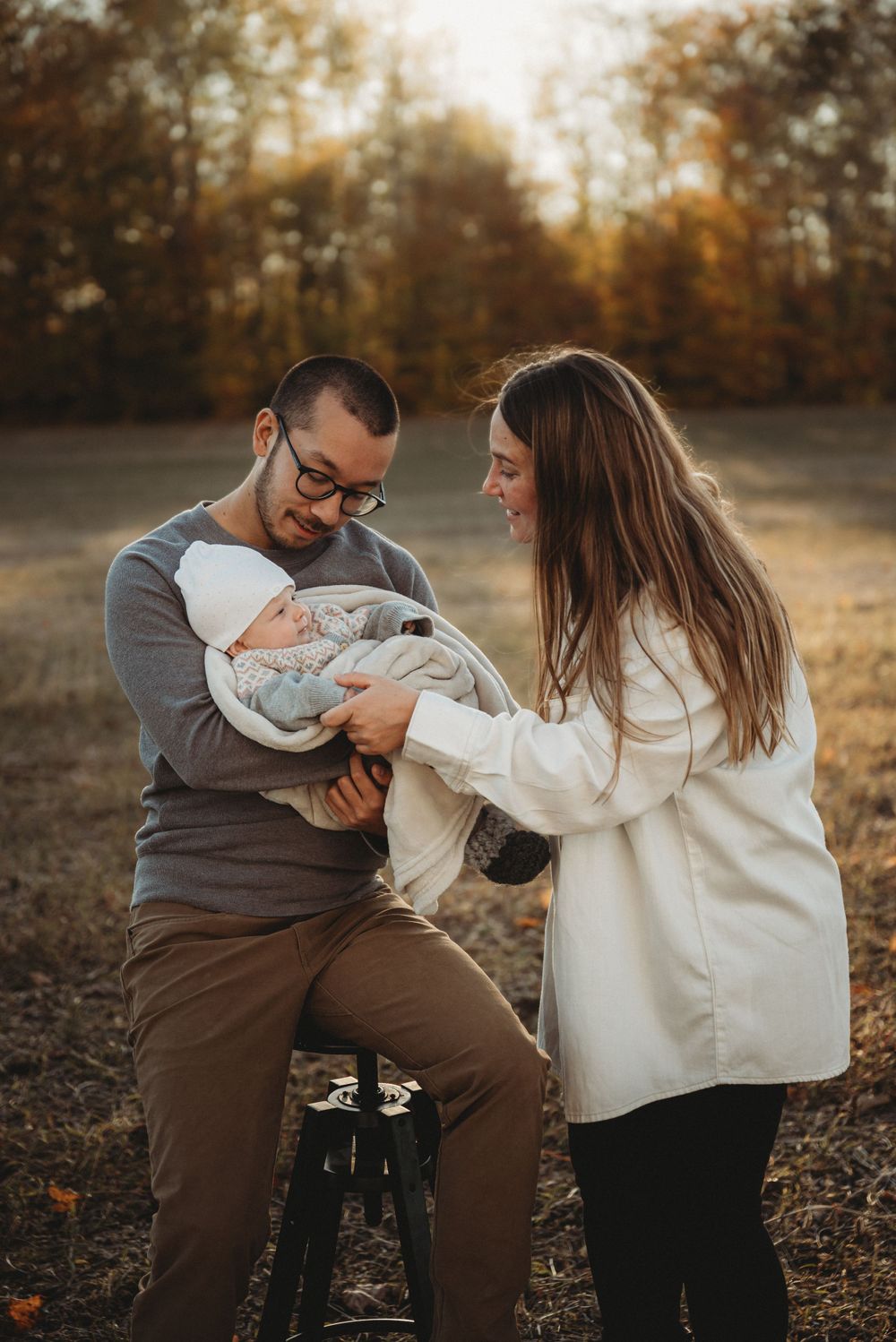 An intimate family moment captured on a rustic stool in a golden autumn field.