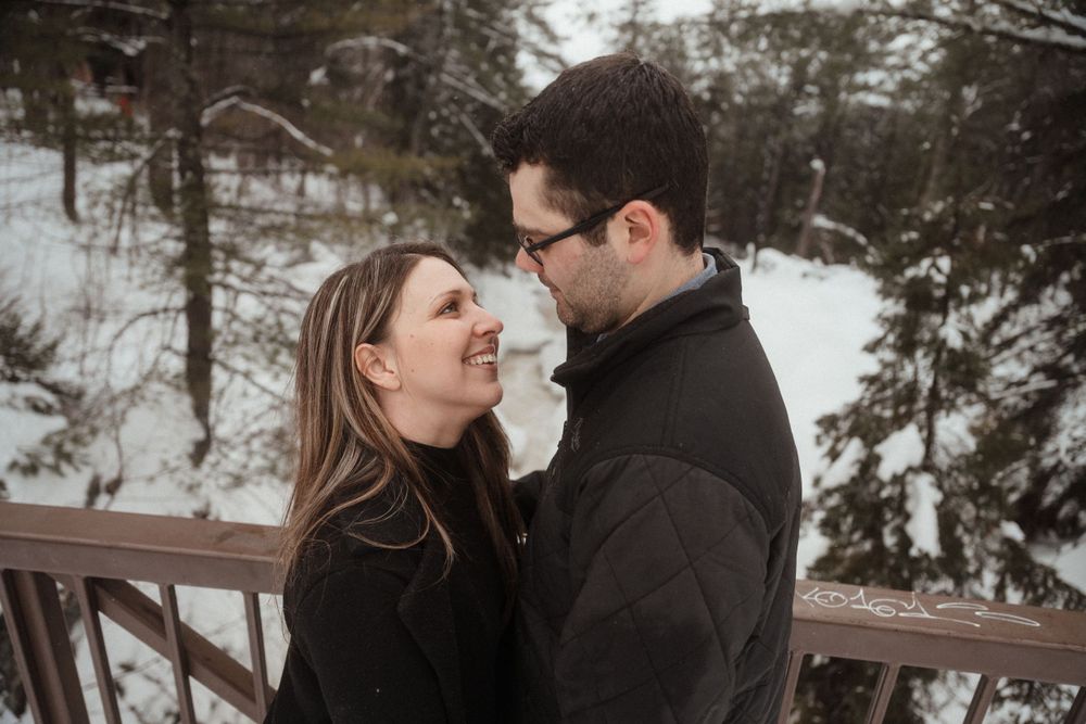 A romantic winter portrait of a couple on a wooden deck surrounded by snowy forest.