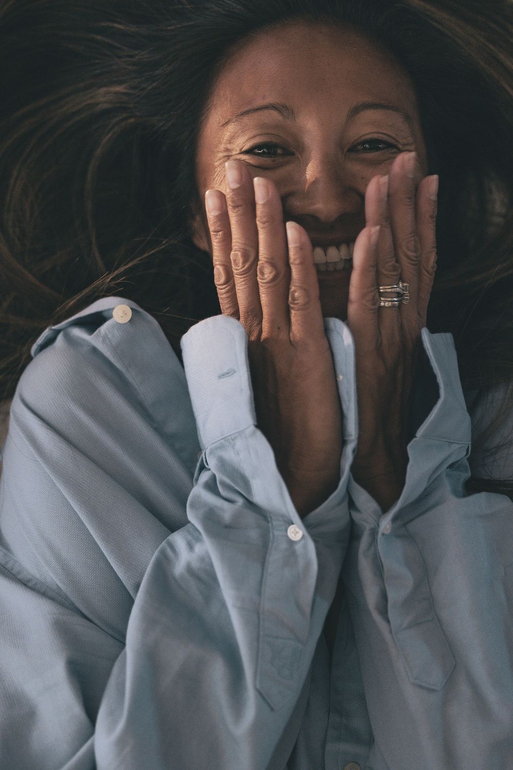 A joyful expression captured in a candid moment with hands covering part of the face, wearing a white button-down shirt.