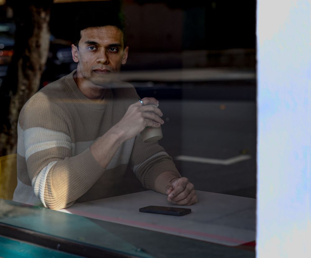 Person sitting alone in cafe seen through window reflection.