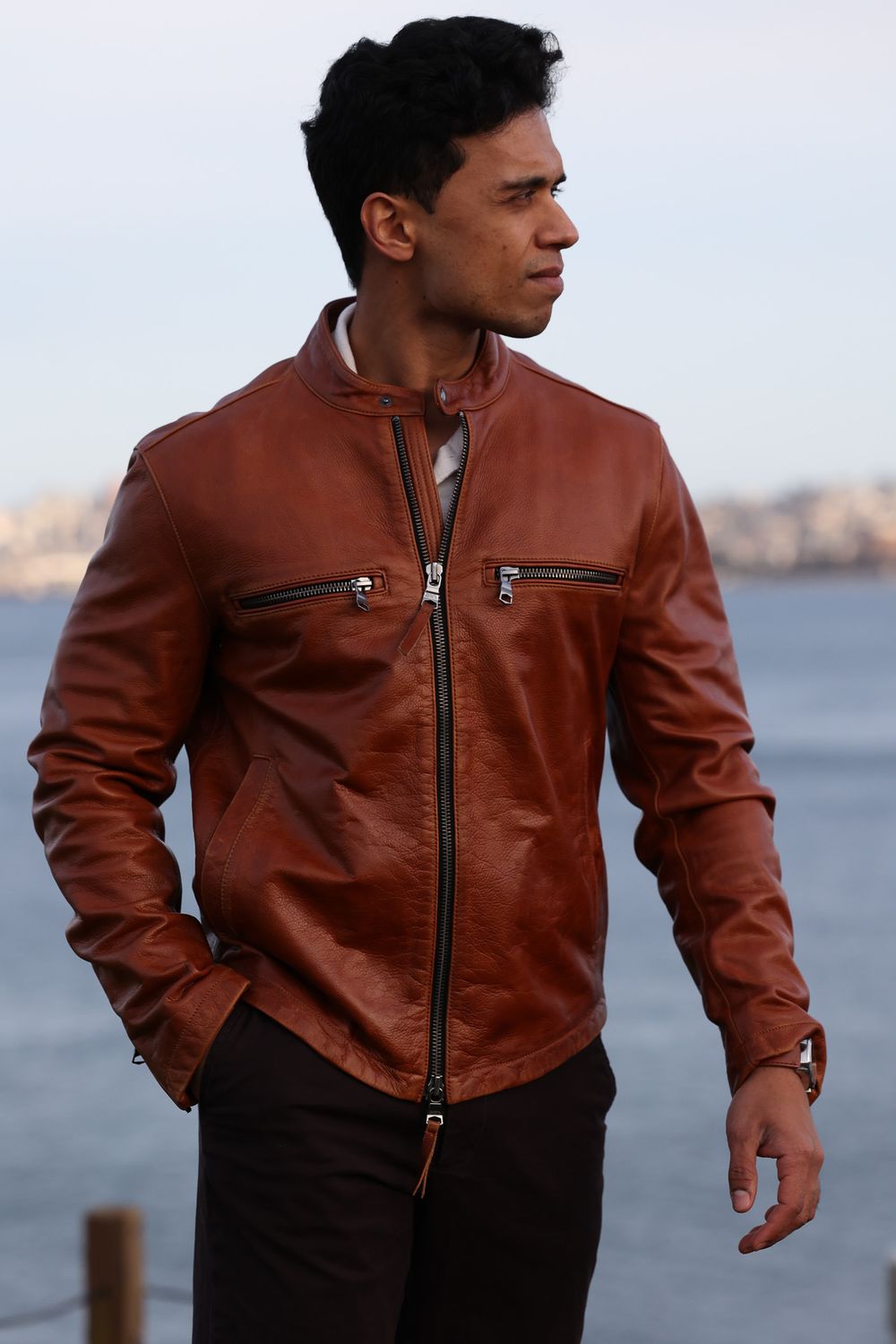 Person wearing brown leather jacket gazing at waterfront cityscape.