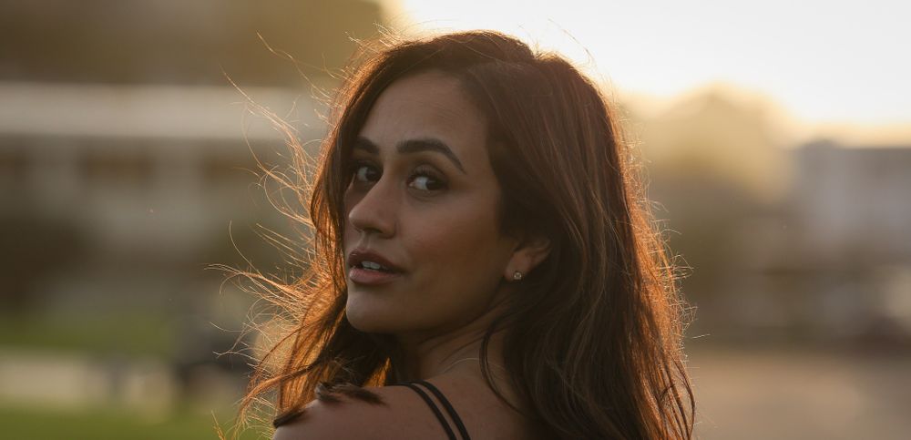 Woman with dark hair illuminated by golden sunset light looking away thoughtfully.