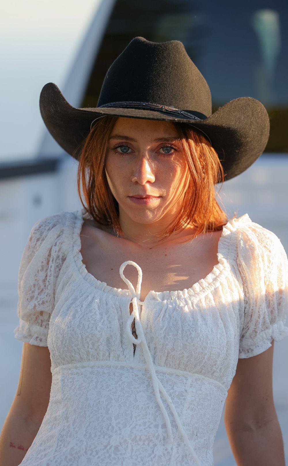 Person wearing cowboy hat and white dress in warm evening light.