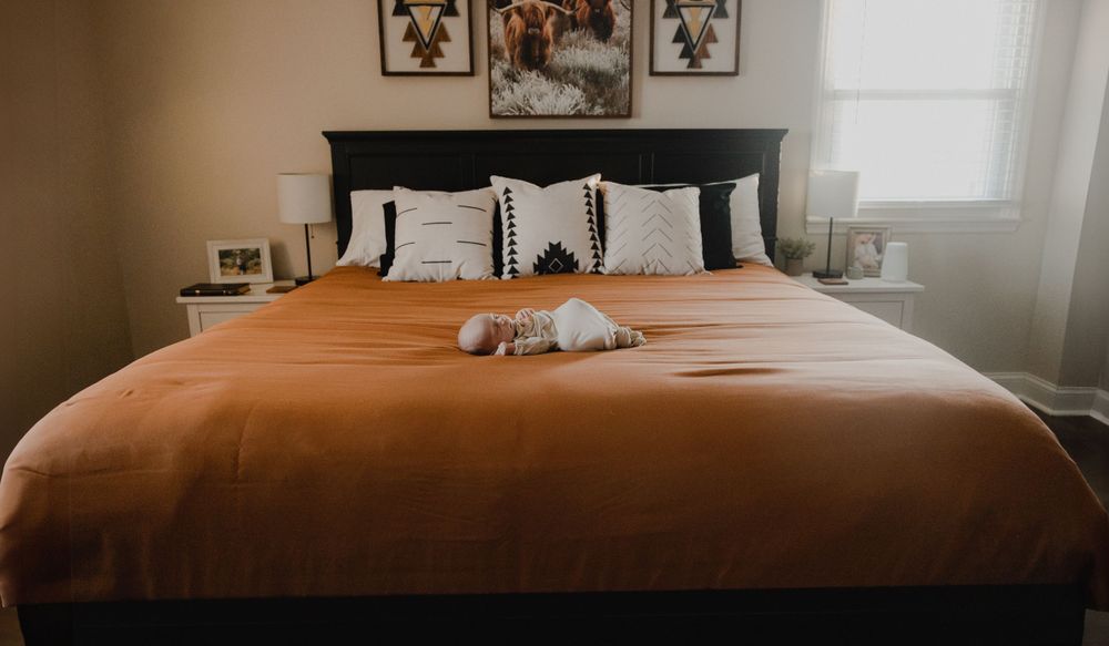 Peaceful sleeping baby on orange bedding with decorative pillows and headboard visible.