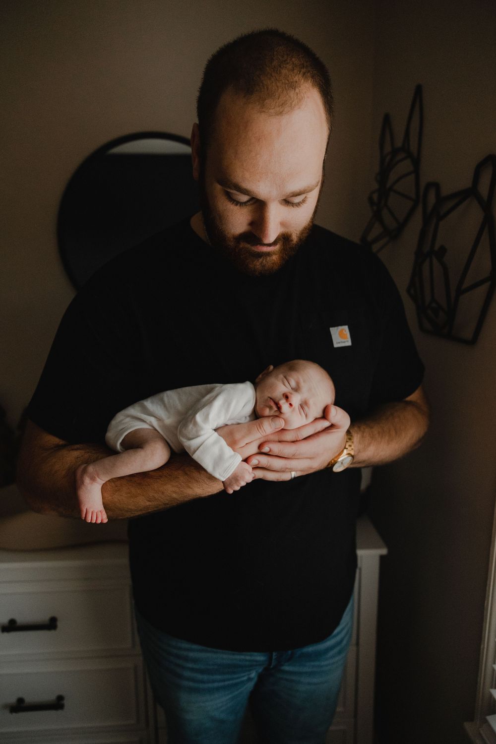 Parent in black t-shirt tenderly holding sleeping newborn baby against dark background.