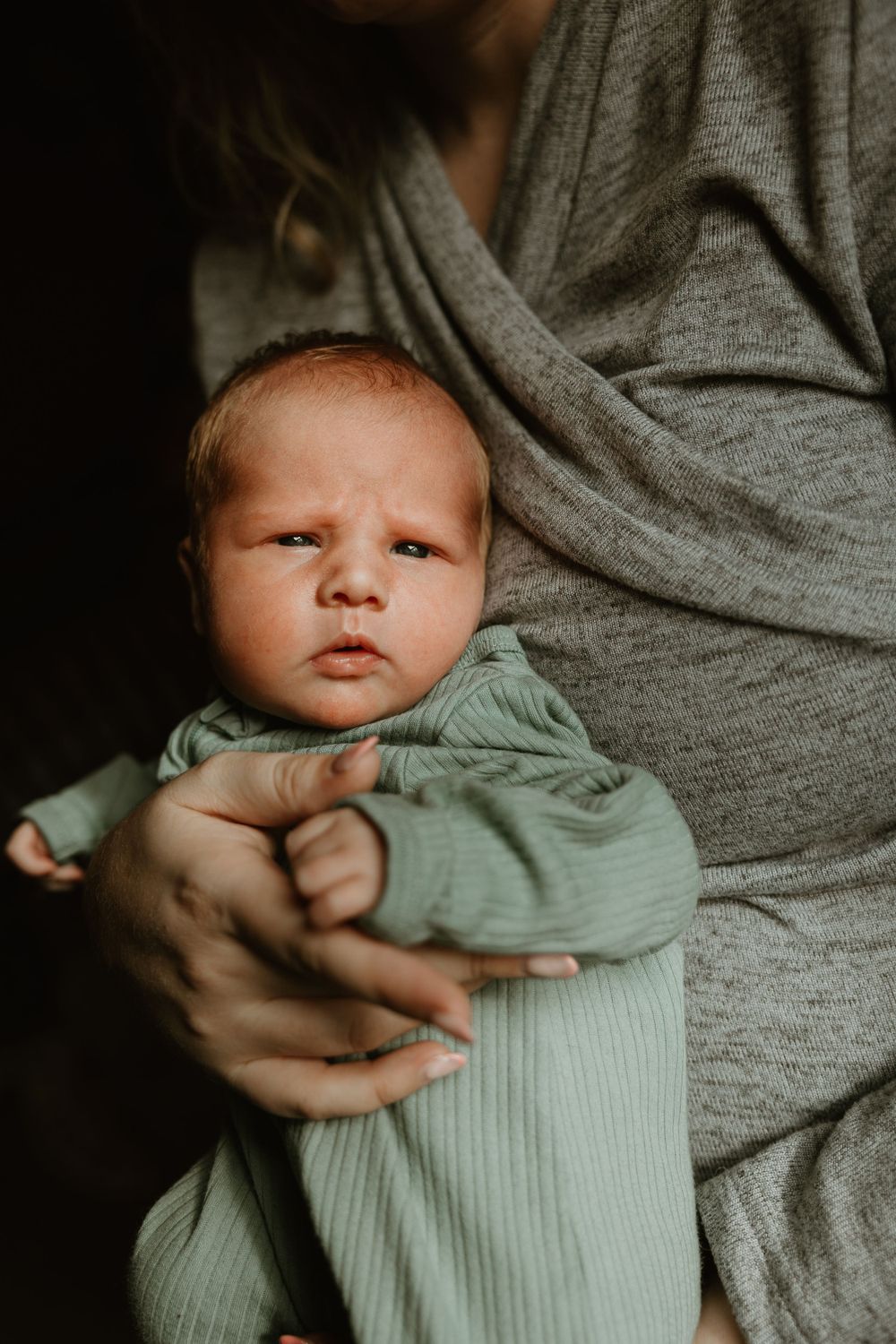 A newborn baby wearing a mint green outfit is held gently in someone's arms.