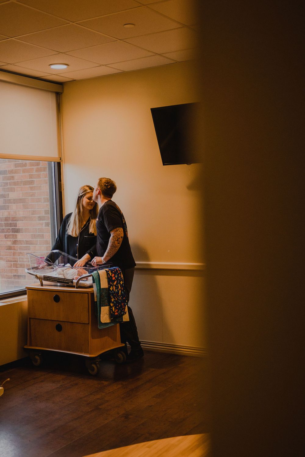 A couple in casual attire checking documents on a medical cart near a window in a dimly lit hospital room.