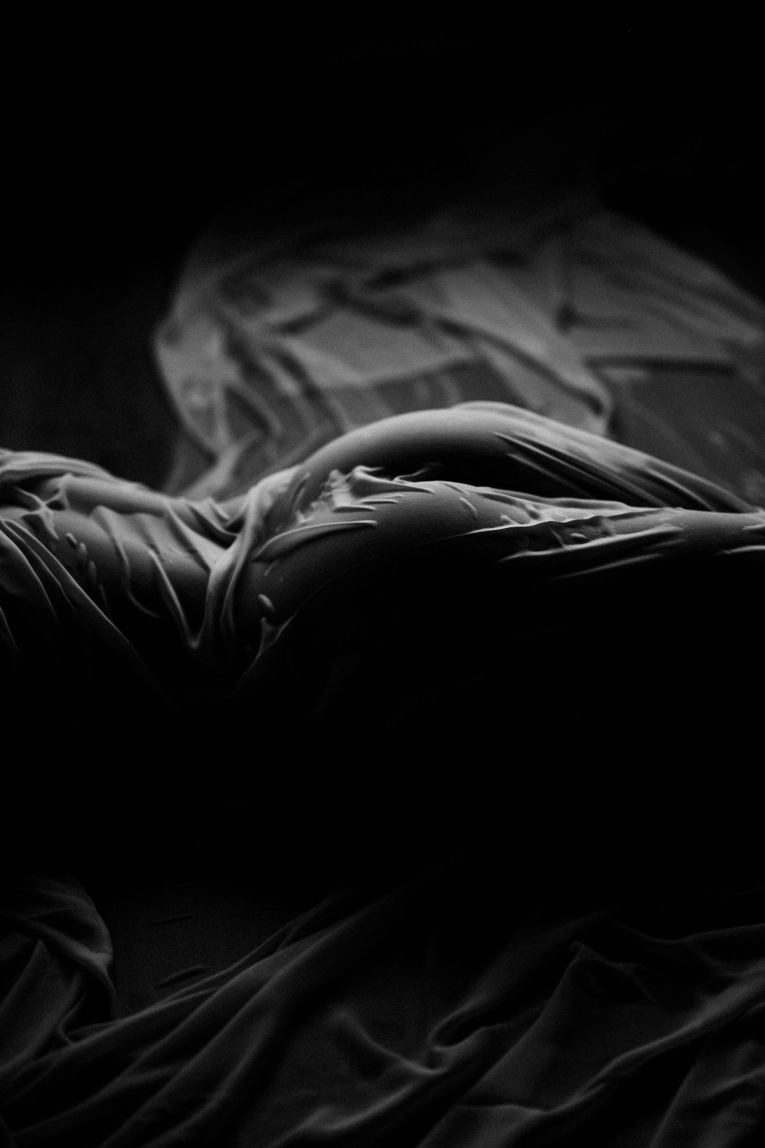 A dramatic black and white photo of rumpled bedding with deep shadows and folds creating abstract textures and patterns.