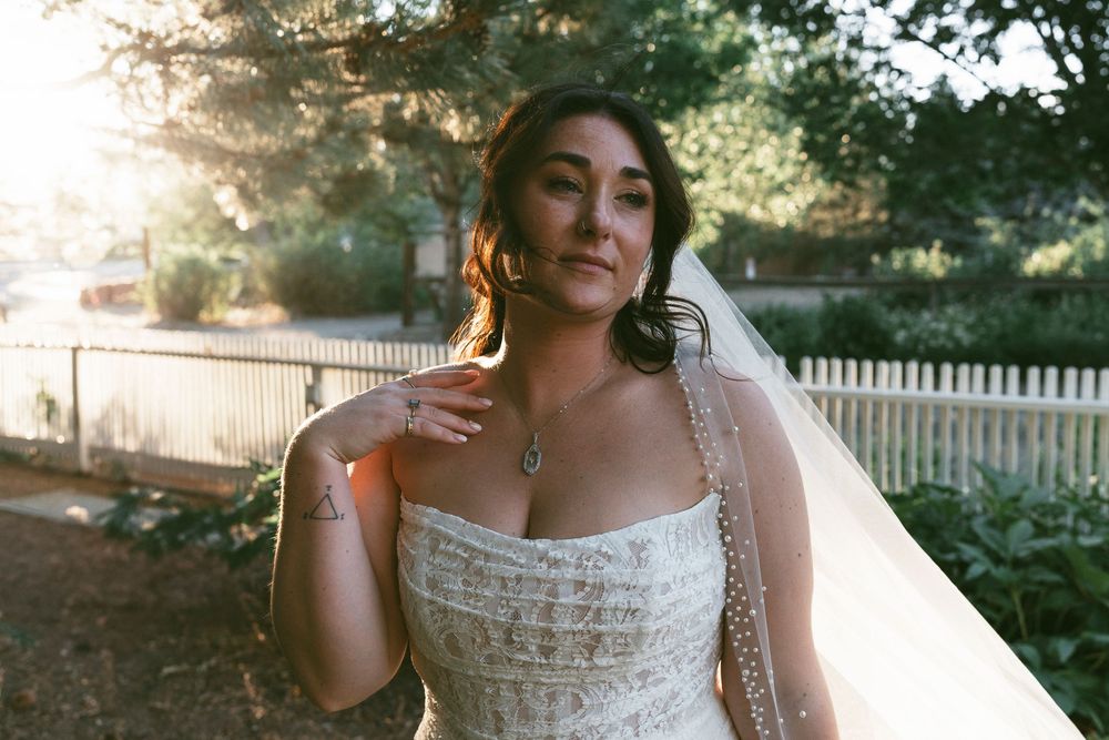 A bride in a white lace dress poses outdoors at sunset with a picket fence and garden in the background in Gardnerville, Nevada